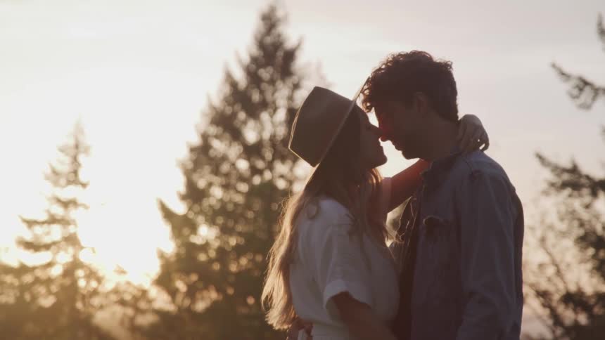 Blonde woman and man hold hands and cuddle in the forest at sunset