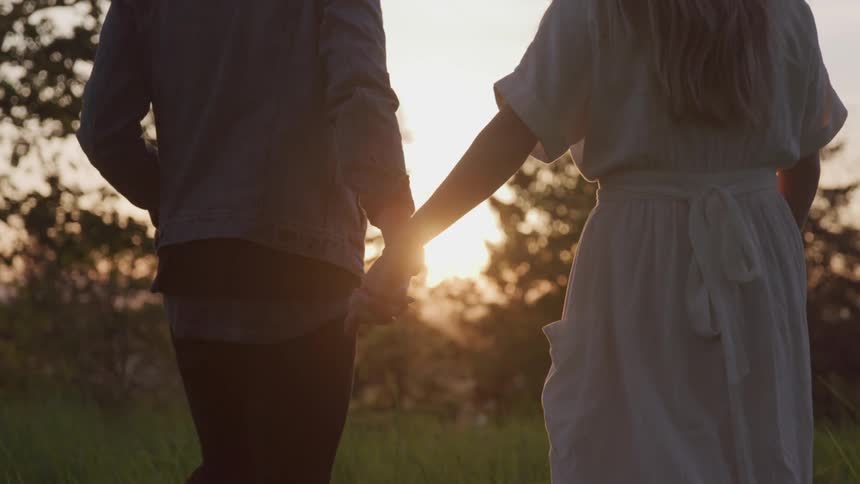 A white couple holds hands while walking through a grassy field