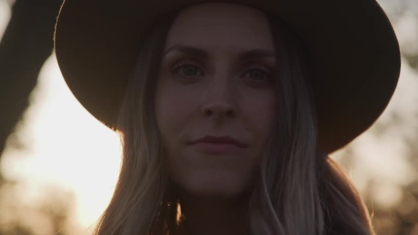 A woman in a hat stands outdoors and looks straight ahead