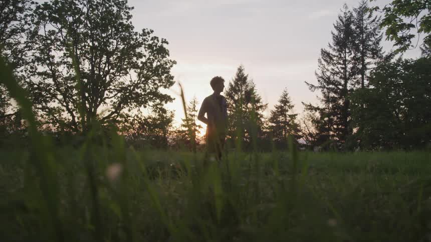 Man stands with hands in pockets in grassy field at sunrise