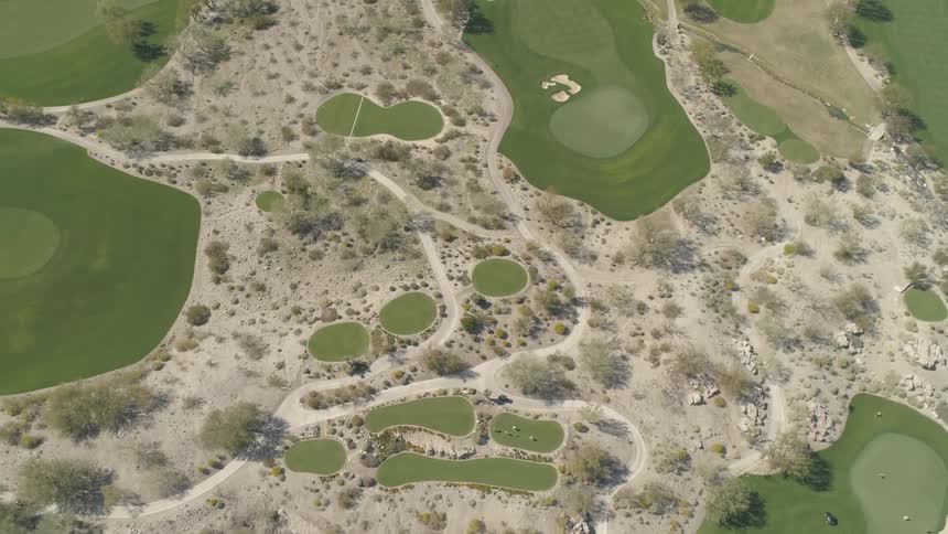 A golf course with lush greens separated by desert terrain
