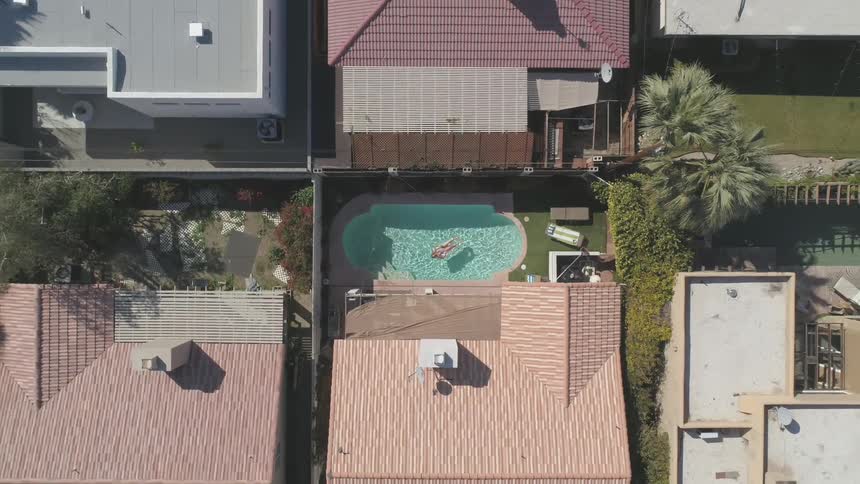 Birds eye view of a woman lying in her swimming pool at home