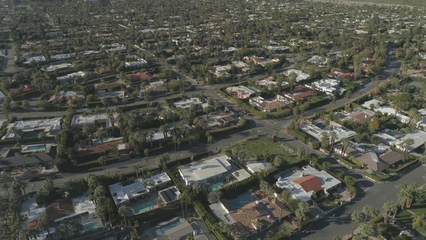 A birds eye view shows a suburban area dotted with trees next to large hills