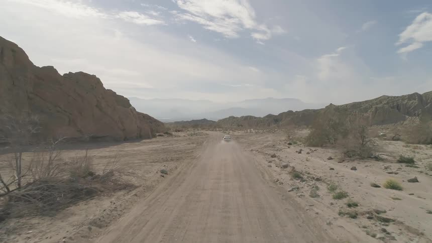 White car goes down on dirt road during daylight