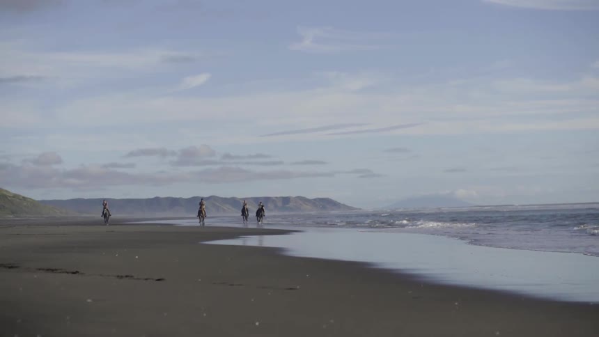 Four people are riding horses on the beach on a cloudy day
