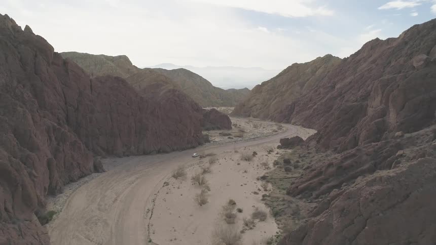 A lone vehicle driving through a dirt valley between mountains