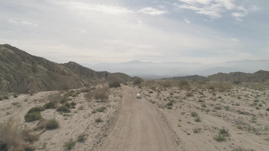 A car travels on a dirt road through a desert landscape