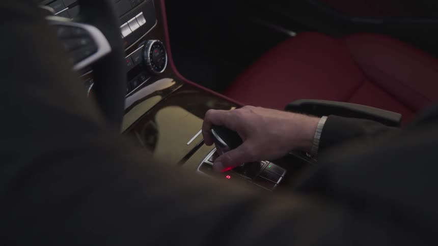 A man has one hand on the gear stick and another on the steering wheel of his sports car