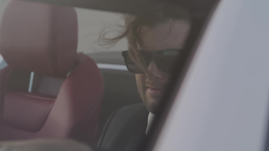 A man wearing a suit drives a car with the windows down