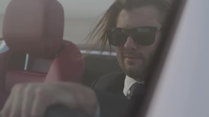 Man in sunglasses and hair blowing in wind while driving convertible