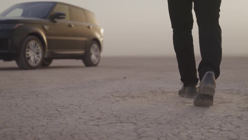 Man walking towards a car parked on desert