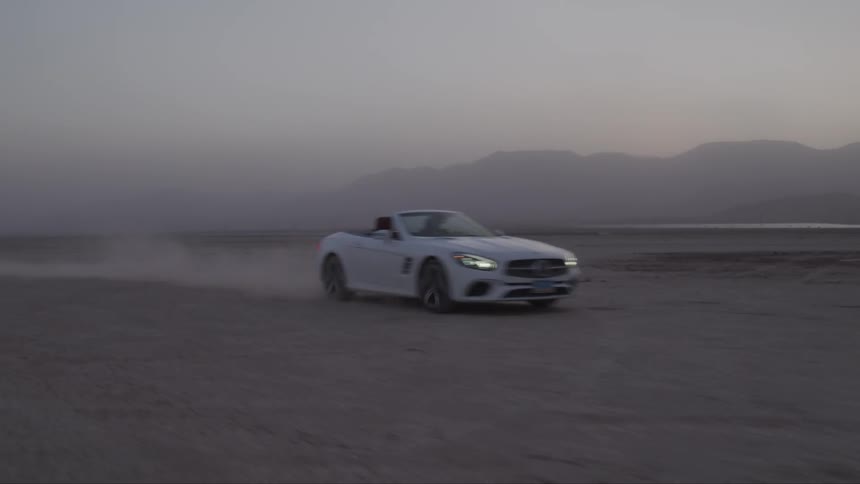 White sports car races through the desert at sunset leaving a trail of dust behind