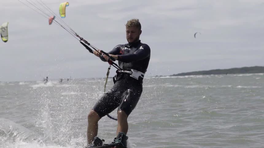 A man kite surfing in the foreground with several others kite surfing in the background on a cloudy day