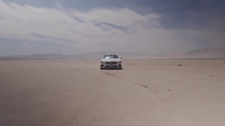 A sporty sedan speeds across a desert plain with mountains in the background