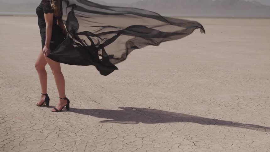 Woman wearing black dress stands in the barren desert during daylight