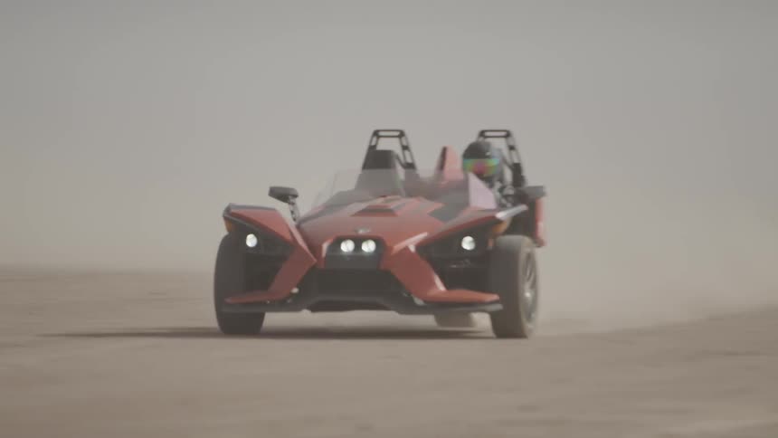 A race car kicks up dust while speeding across a dirt field