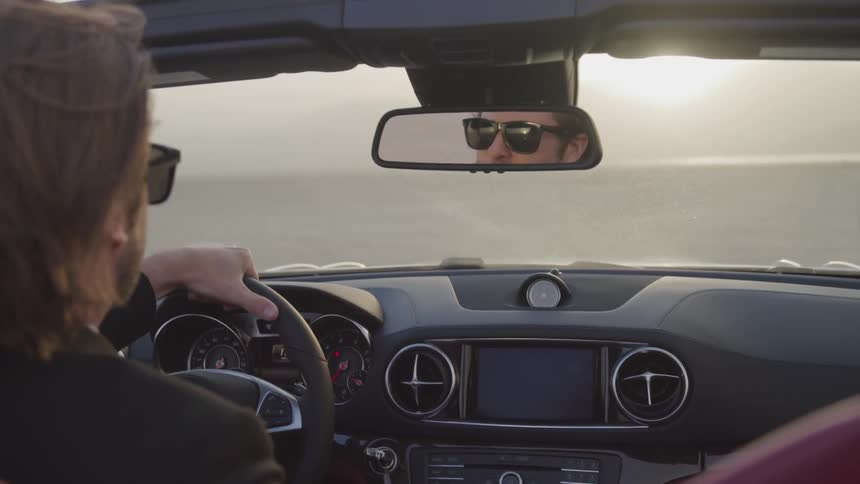 A white man wearing sunglasses drives a car through the desert