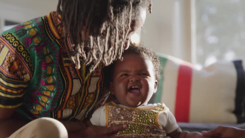 A dad holds and rocks his laughing daughter as his wife laughs along