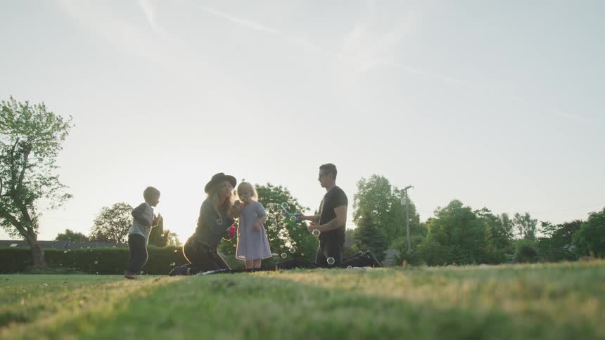 Husband and wife kneeling on the grass playing with bubbles with their son and daughter