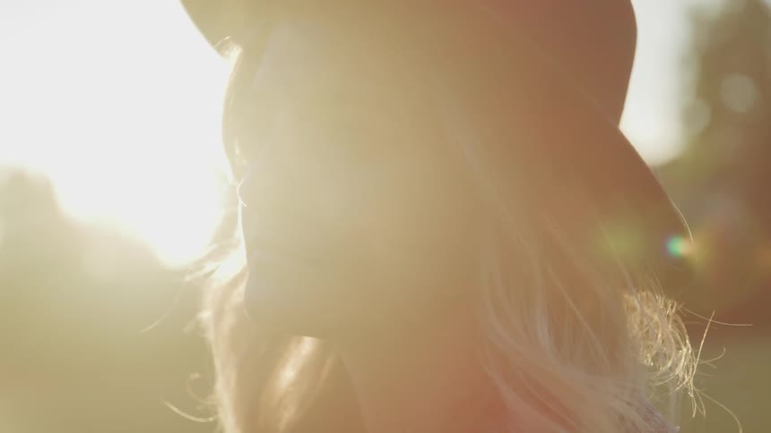 A beautiful woman wear a black hat with sun flare behind her