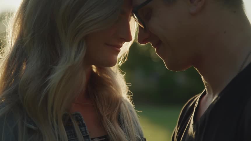 A man and a woman stand close together in sunlight