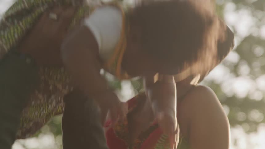 A woman laughs and smiles while a man is lifting a chubby baby up and down into the air