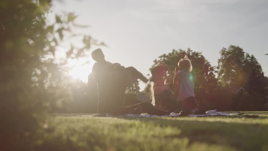 A couple play with their young children while sitting on a blanket in the park