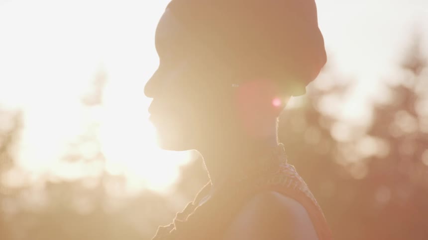A woman standing outside with the sun and trees in the background