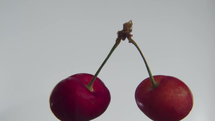 A pair of cherries are dropping to the ground