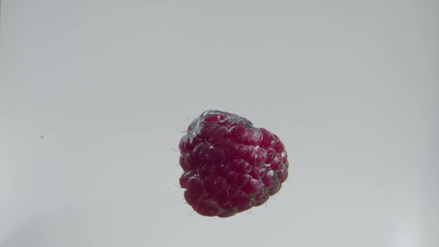 A raspberry falling through a clear liquid