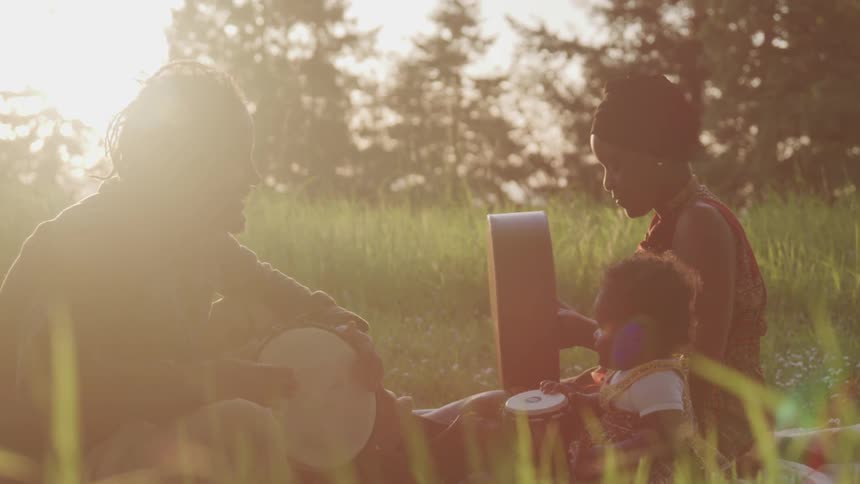 A family sit in the grass playing small drums