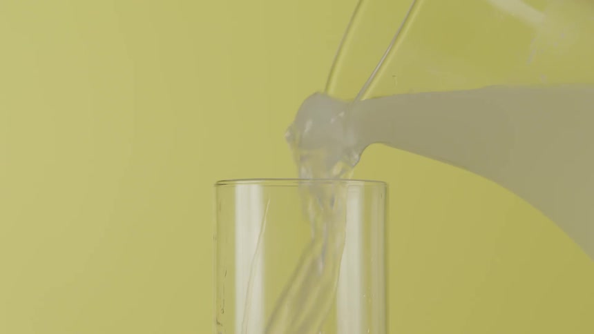 Lemonade with ice is poured from a clear pitcher into a clear glass