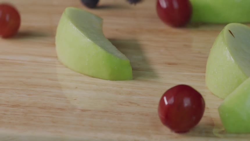 Apples grapes strawberries and blueberries are dropped onto a wooden surface