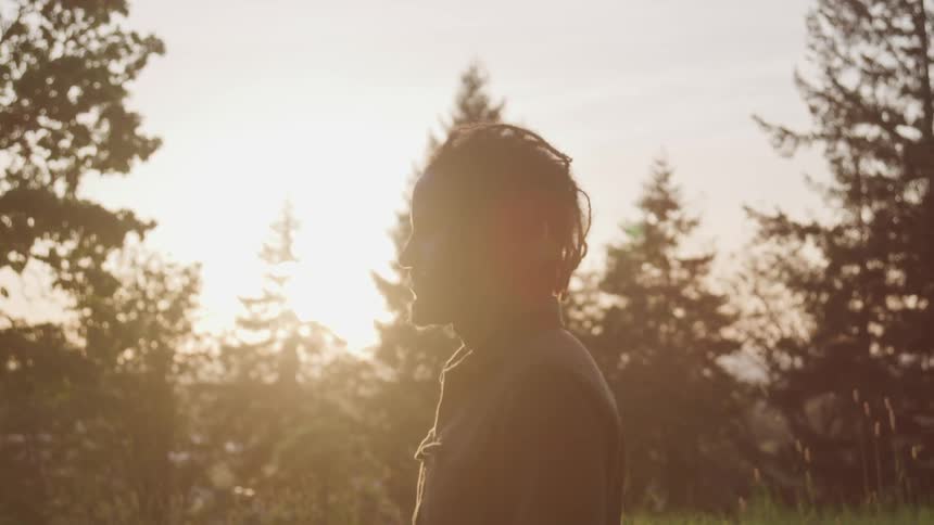 Black man stands in the forest while the sun goes down