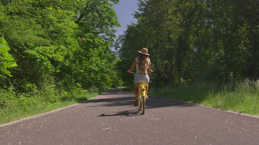 A woman rides a yellow bicycle on a paved road in the summer
