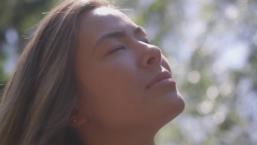 A woman standing outside with her eyes closed and the sun shining on her face