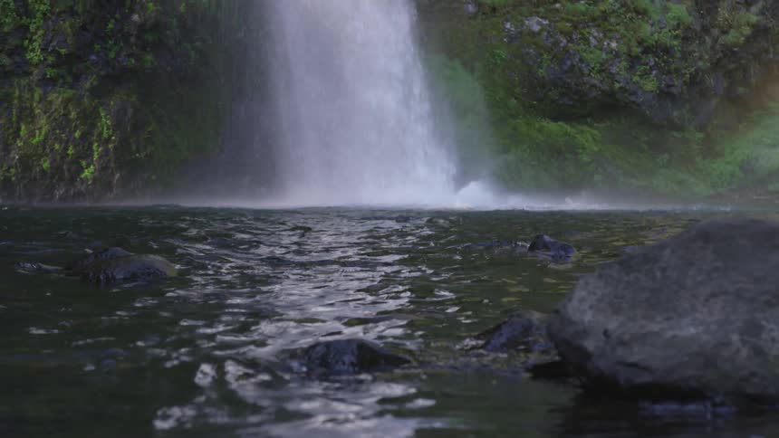 Water flows and splashes down from a waterfall causing a rainbow in the air