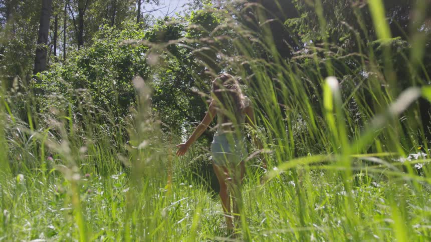 A young white woman walks through a grassy field