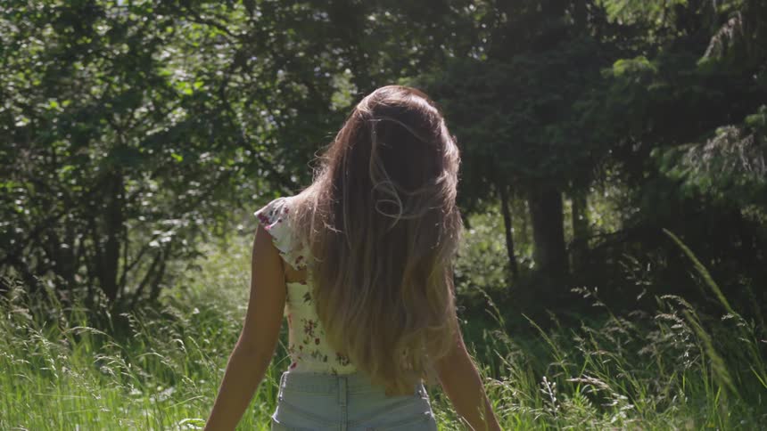 Caucasian female with very long hair walking in tall grass and trees