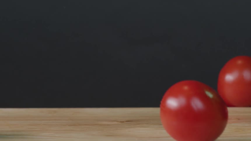 Four tomatoes being dropped onto a cutting board