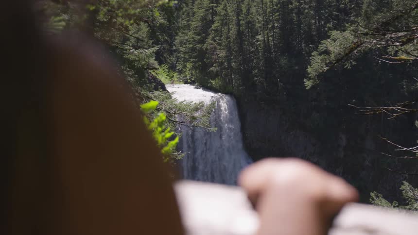 A person looks at a large waterfall in a forest