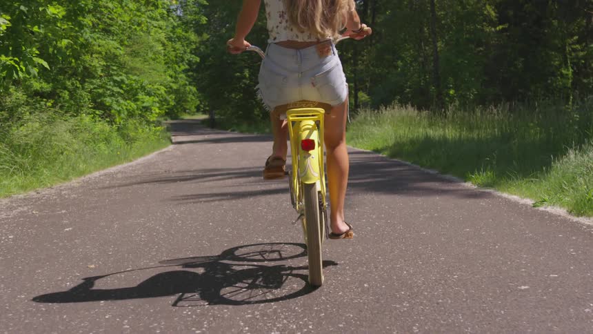 Woman wearing shorts cycle on the asphalt road in the forest during daylight
