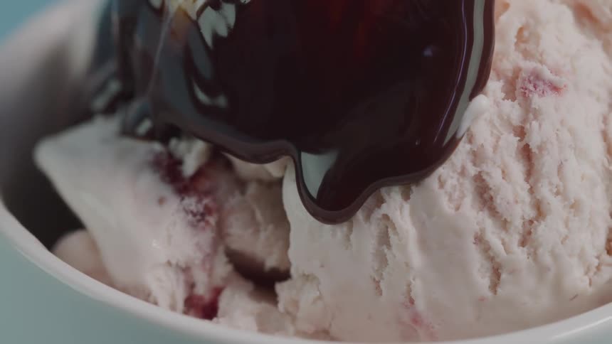 Chocolate sauce going over a bowl of ice cream