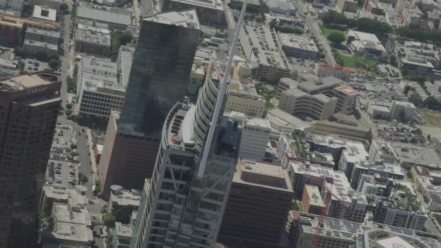 A skyscraper with a large white antenna is shown up close in a birds eye view of an urban area
