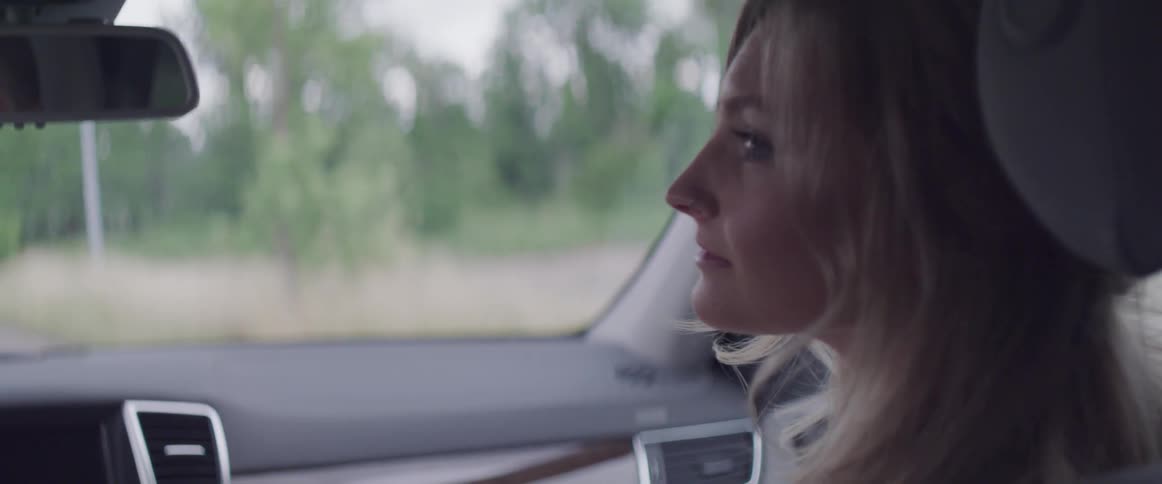 A woman riding in the passenger seat of a car turns her head and looks at the driver then looks back out the window