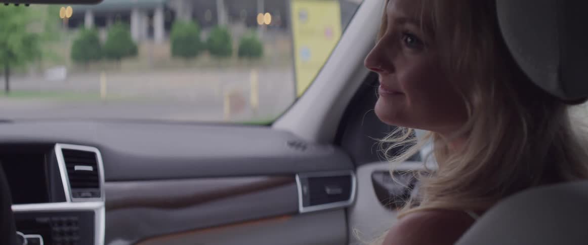 Woman sits in passenger seat of moving vehicle smiling toward drivers side