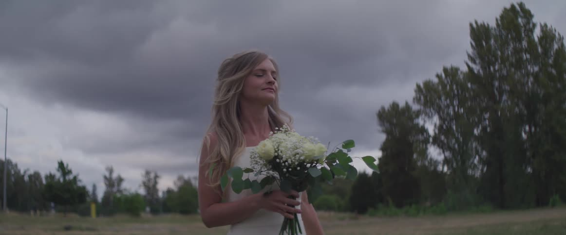 A woman in a white dress holding a bouquet of flowers walks through a field