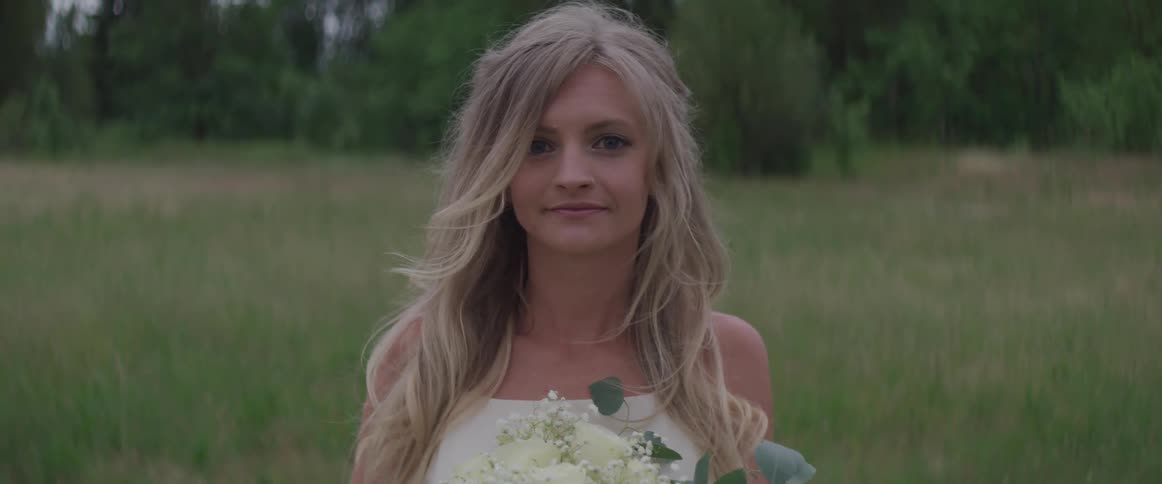 A woman wearing a white dress holds flowers while standing in a grassy field