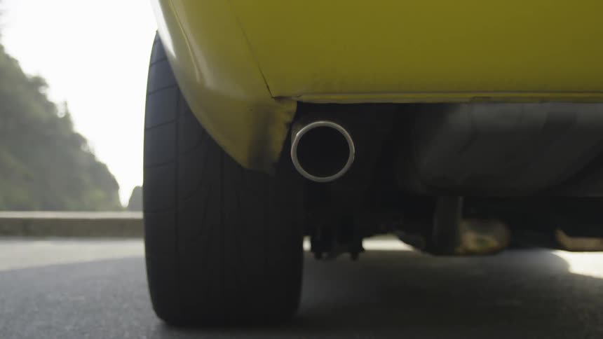 The exhaust of a yellow car shakes while parked on a road