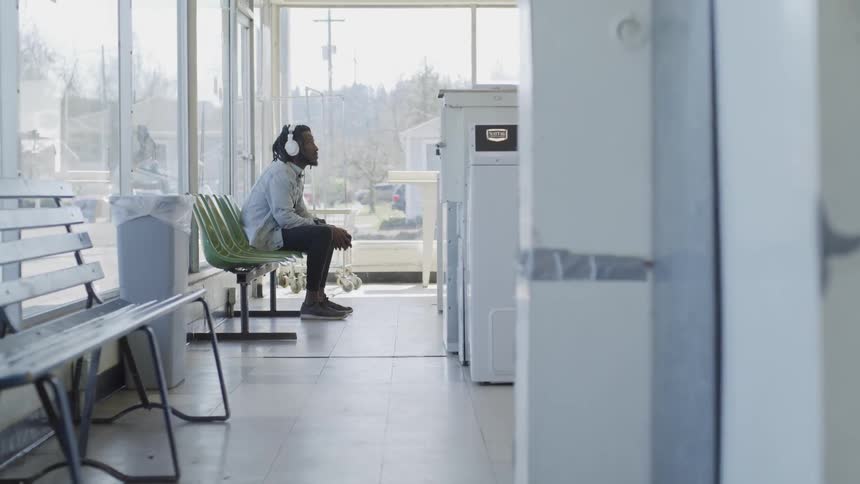 Man wears headphones as he sits in a laundromat